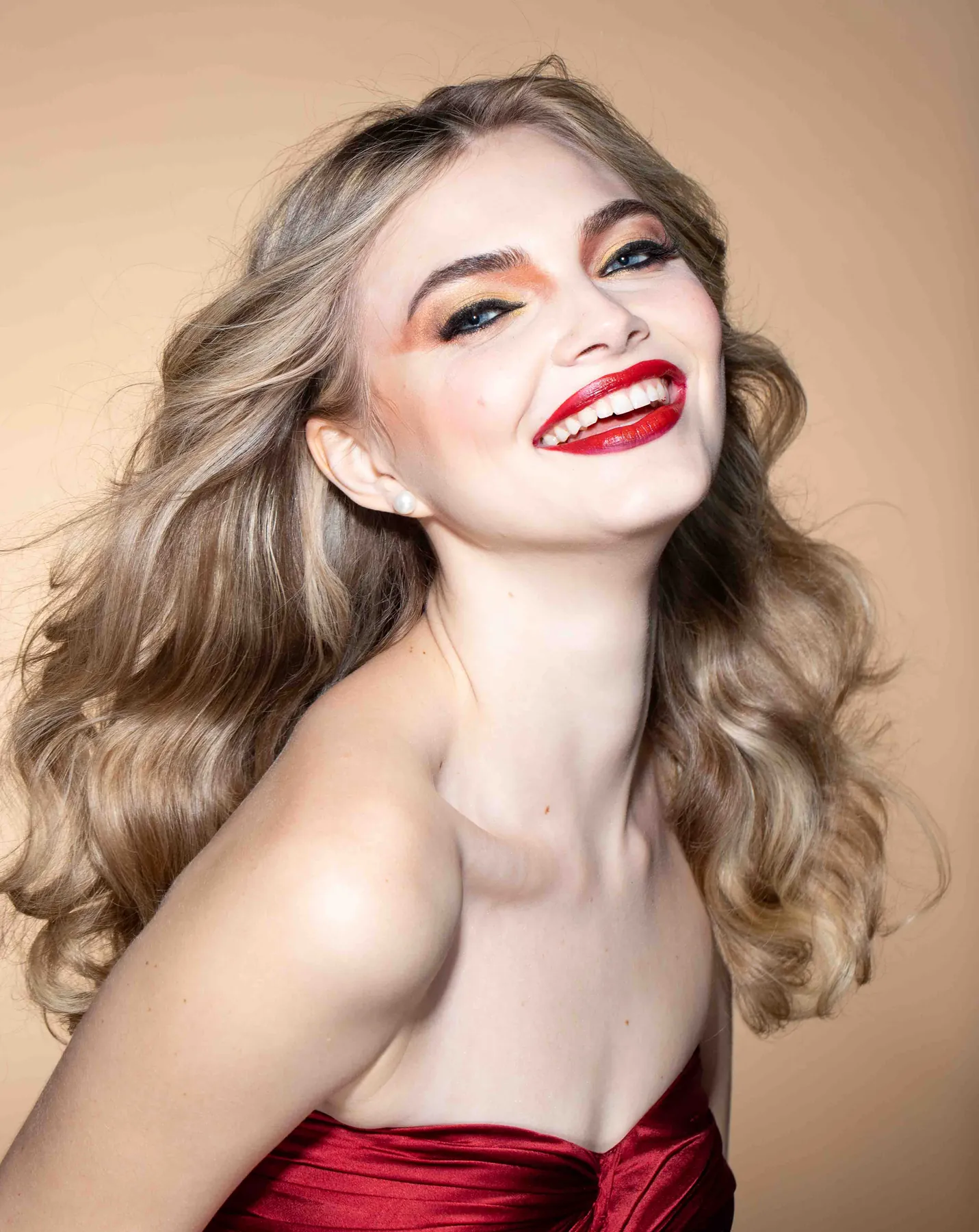 Beauty portrait of a laughing model with soft blonde curls, bold red lips and warm copper eye makeup
