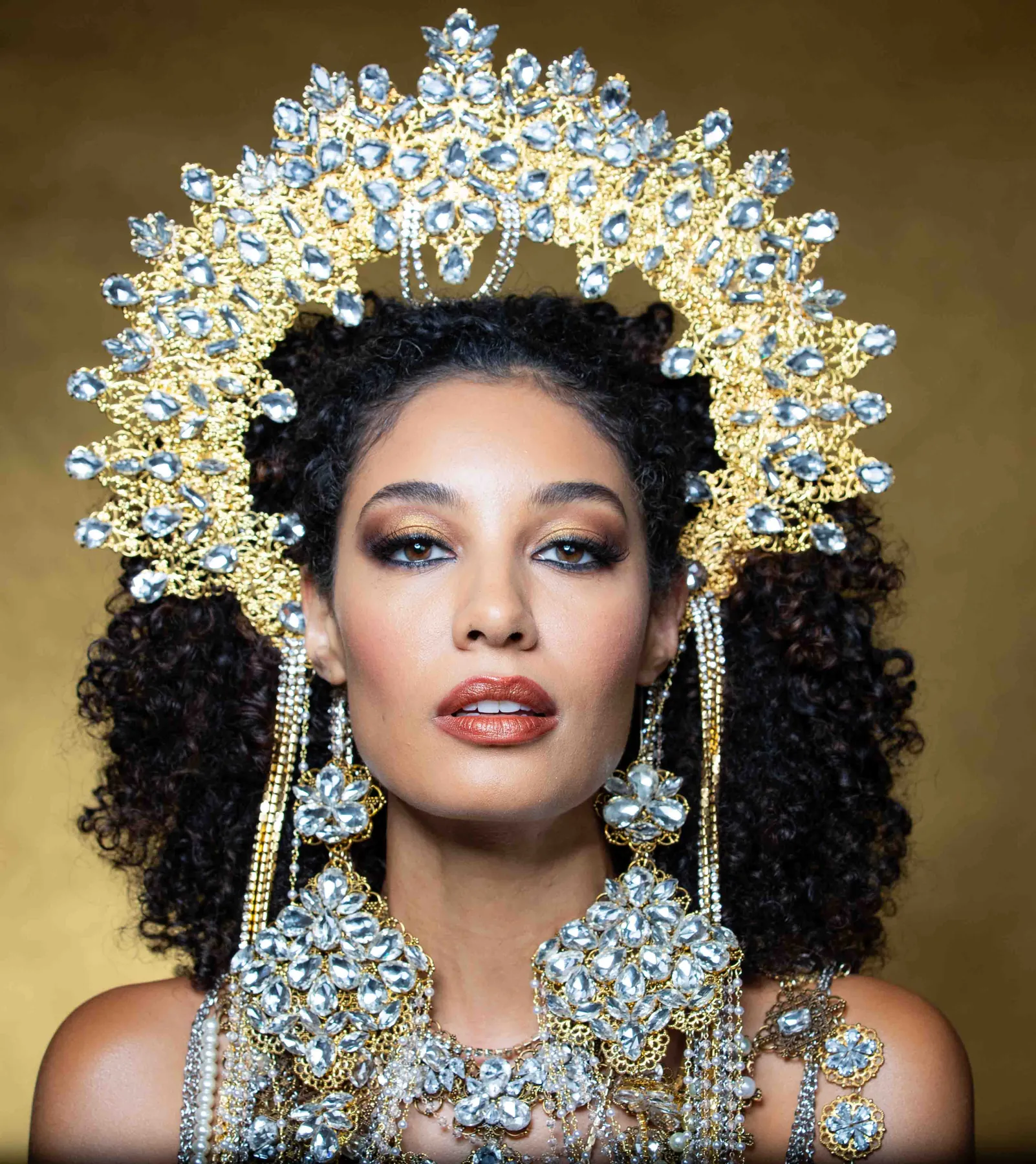 Model wearing an ornate gold and crystal halo headpiece with long chandelier earrings