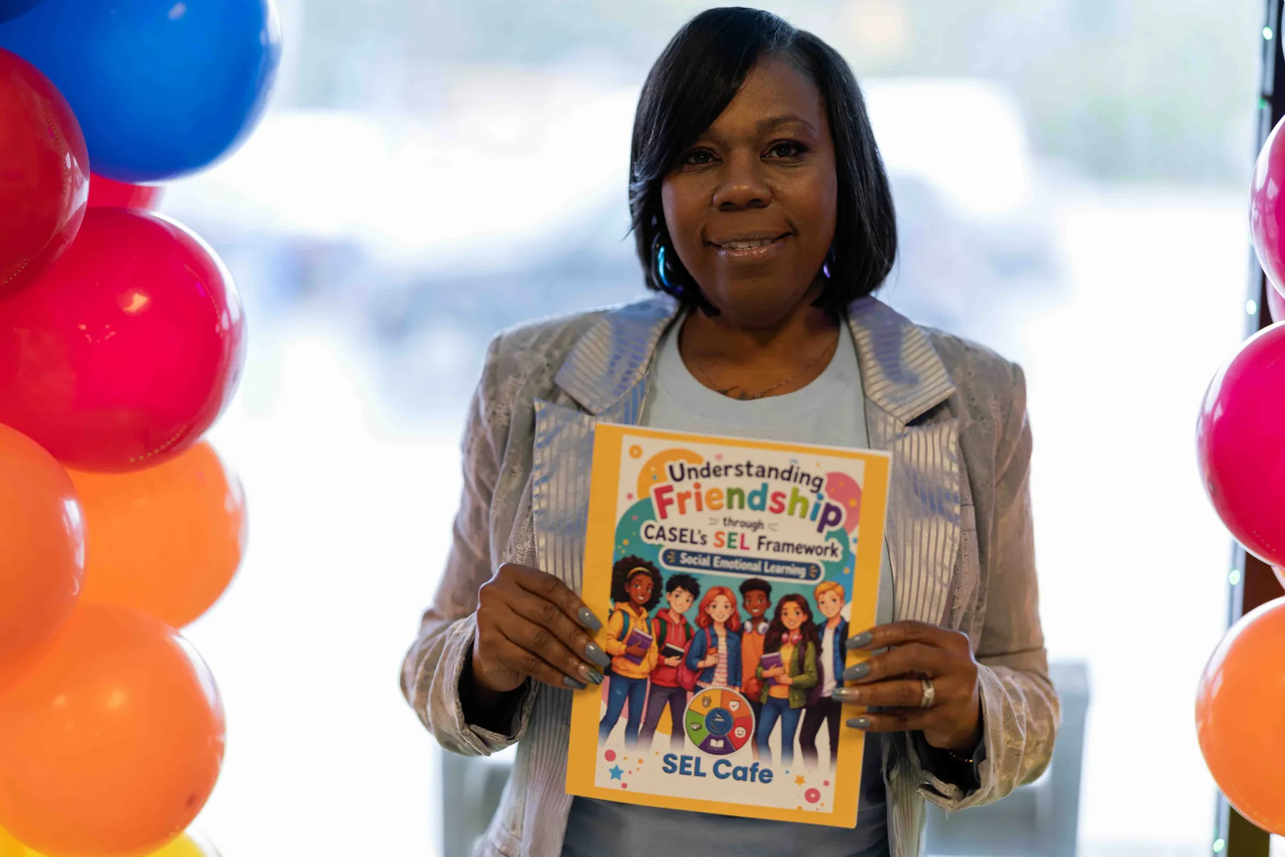 Author holding up her children's book at a book signing, surrounded by colorful balloons