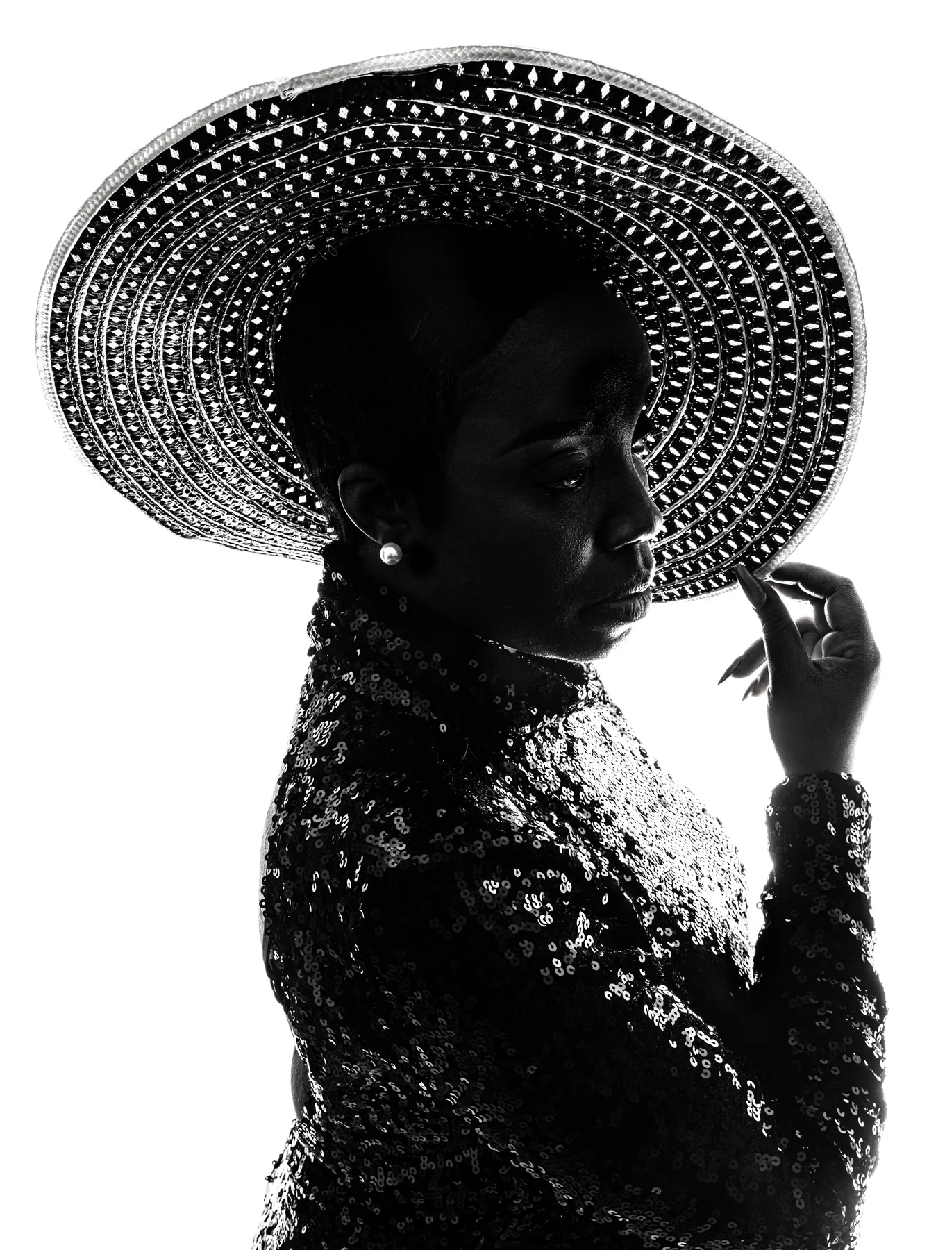 Black silhouette of a model in a wide studded hat and sequined jacket against a pure white background