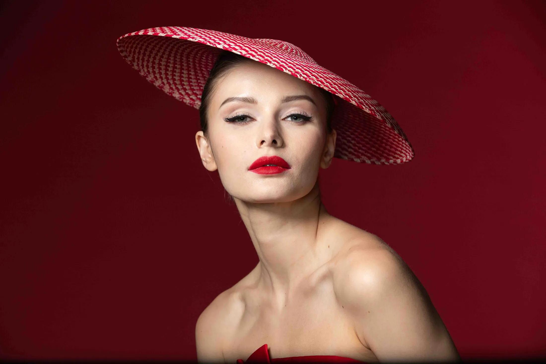 Model in a red dress and a wide red hat against a deep red backdrop